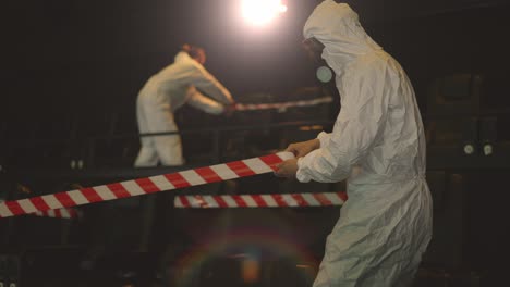 quarantine due to coronavirus pandemia - two men in protection costume stretching warning ribbons over seats