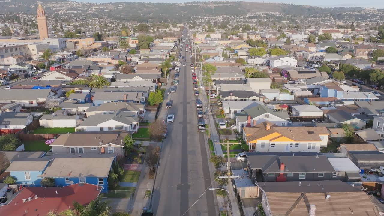 Aerial footage slowly flying down a street in a neighborhood during sunset in Oakland, California with cars driving down the street.