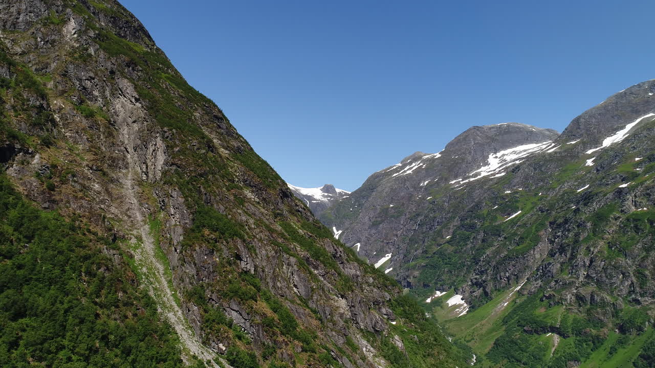 드론은 노르웨이 서쪽 해안에서 녹색과 눈으로 인 산꼭대기와 함께 바위 산 절벽을 드러니다.