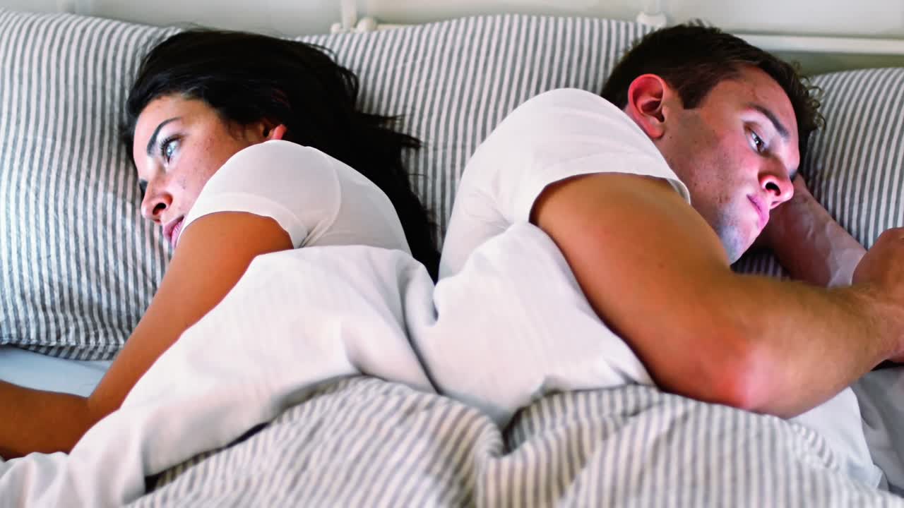 Couple using digital tablet and mobile phone while lying on bed