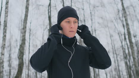 un joven que corre por la mañana sostiene auriculares en sus manos y se los inserta en los oídos antes de correr en el parque. carrera de invierno. utilice dispositivos y aplicaciones de formación modernos. escuchar música mientras entrenas mientras corres