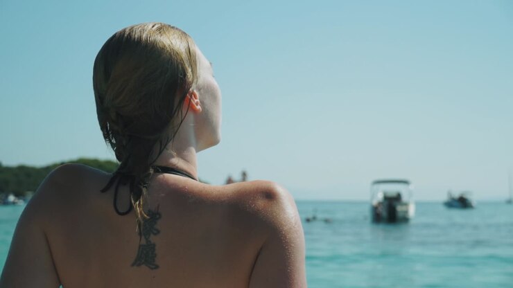 Giovane donna con tatuaggio sulla schiena che prende il sole su una barca