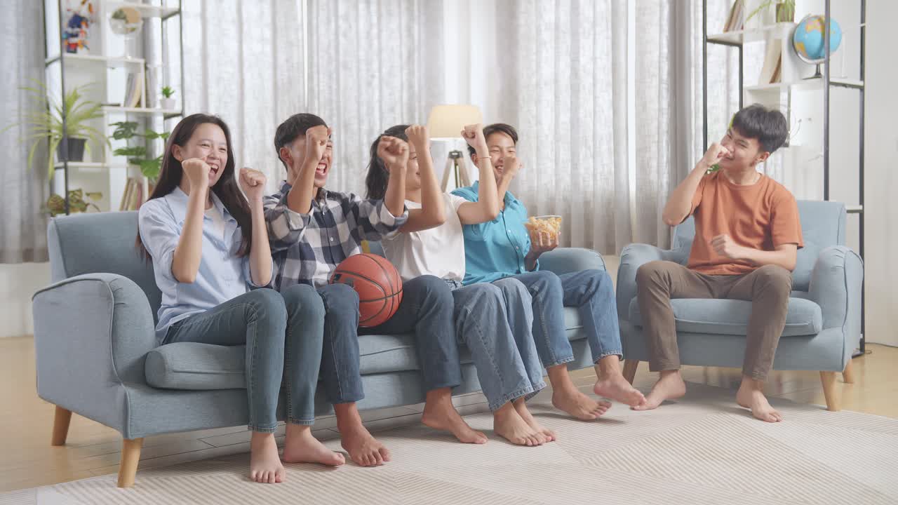아시아 십대들이 농구 경기를 tv에서 지켜보고 집에서 승리를 축하하고 있습니다.