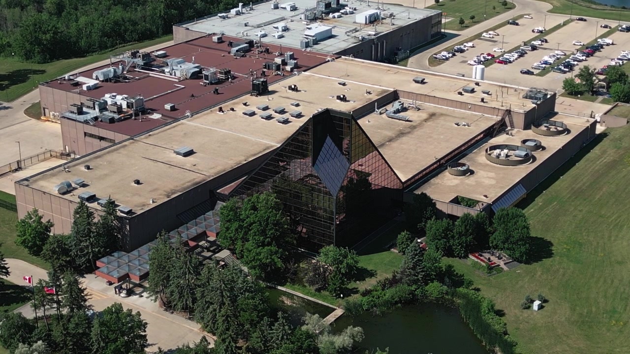 Telefoto droneoptagelse, der kredser om glasindgangspavillonen ved Royal Canadian Mint i Winnipeg på en solrig sommerdag.