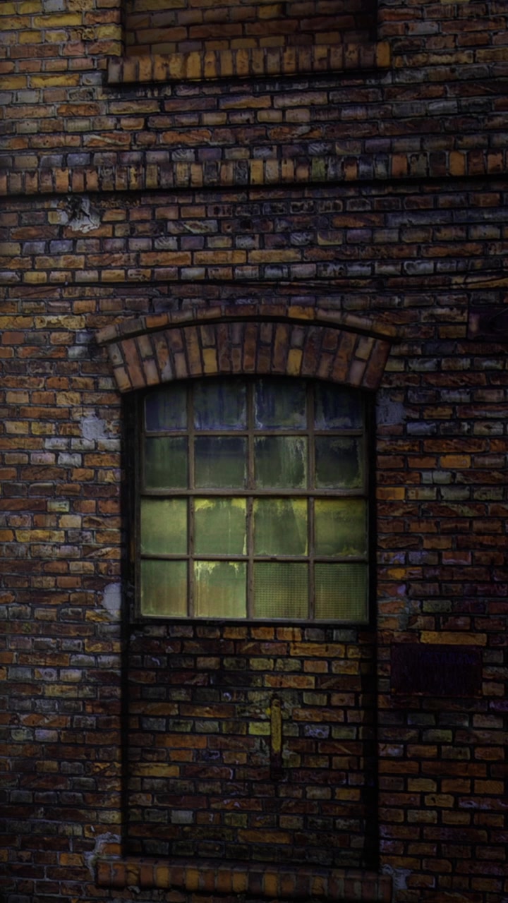 Vecchio muro di mattoni con una finestra alla luce della sera in un contesto urbano.