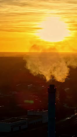 gases rise from an industrial chimney against a golden sky at sunset. vertical shot.