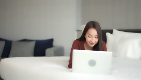 brunette female lying on a bed using her laptop and surfing the internet or checking her social media