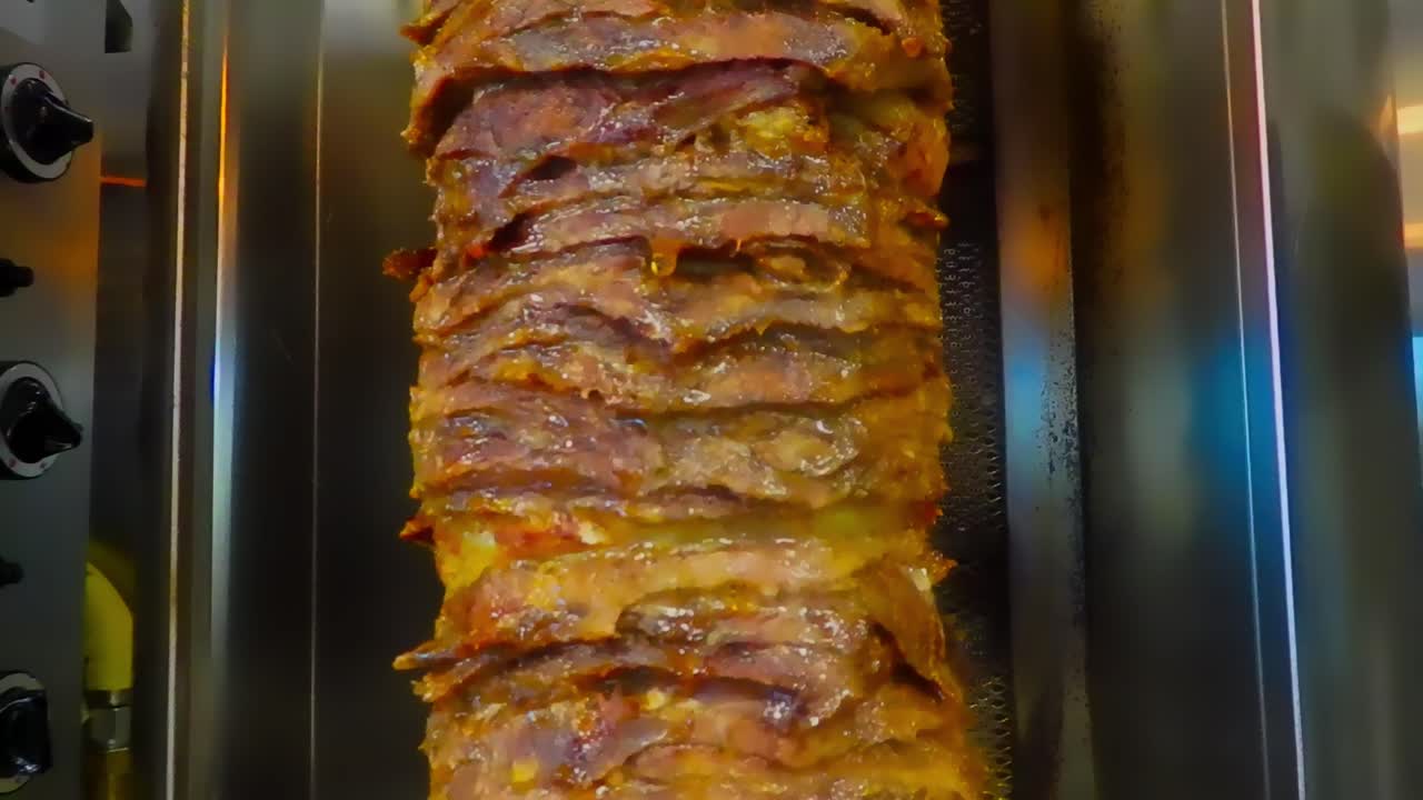 bucle continuo 1de5 primer plano de bistecs apilados cortados en rodajas finas sobre una barbacoa vertical marinada y los jugos fluyendo hacia abajo con la carne de res shawarma al estilo árabe en una plataforma de cocción flameada de acero inoxidable