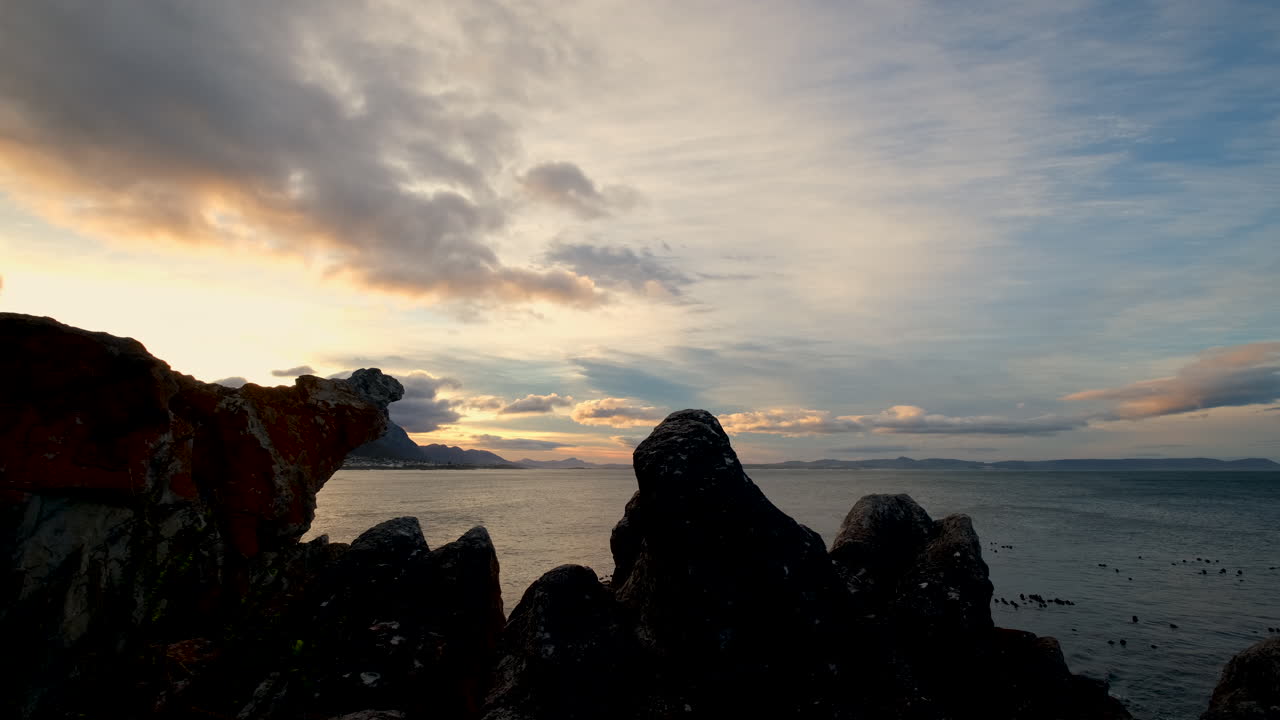 Scenic sky with clouds at sunrise over ocean with silhouette of coastal rocks