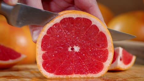 male hand with a knife cut pieces of ripe grapefruit.