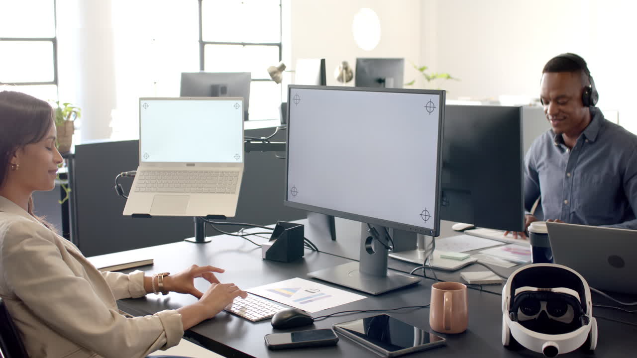 Working in modern office, woman using desktop computer and African American man wearing headset, cop