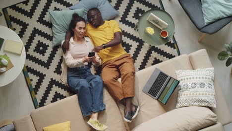 diverse couple resting on floor and using smartphone