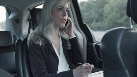 businesswoman talking on phone and writing notes in a car