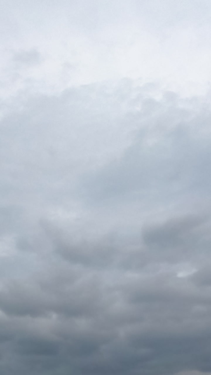 Grey rainy cloudscape in the sky. Dramatic clouds spreading in the atmosphere. Low angle view. Timelapse. Vertical video