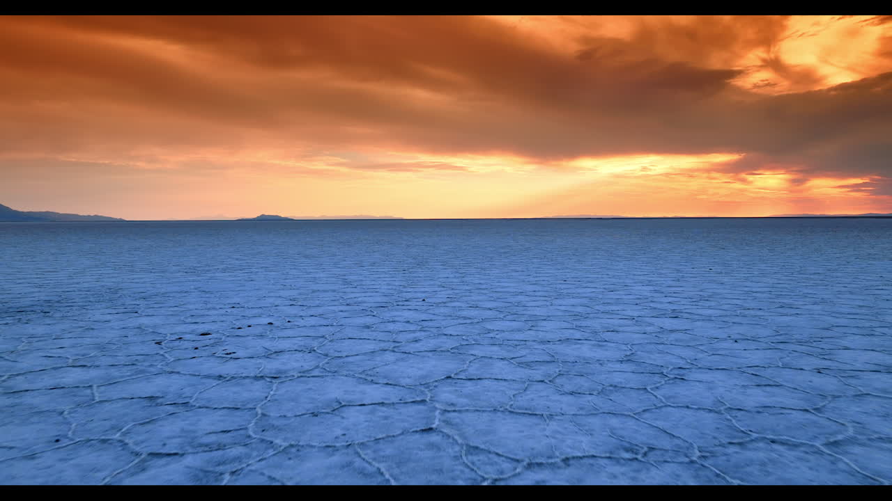 Lonely man walking by the salty land approaching camera. Cloudy orange sky at backdrop. Bonneville Salt Flats, Utah, USA at sunset time