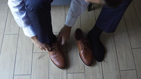 man tying brown leather shoe on tiled floor during wedding day preparations, close-up