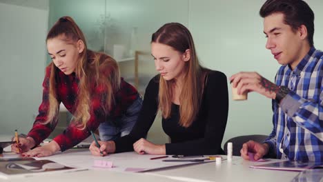 grupo de jóvenes diseñadores de interiores trabajando juntos en una oficina creativa. jóvenes profesionales haciendo bocetos sentados en la mesa, preparando su nuevo proyecto y bebiendo café en cámara lenta