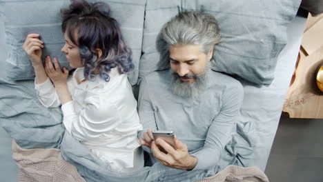 couple in bed, one using smartphone