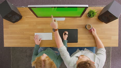 overhead view of male and female graphic designers working at computer with green screen in office