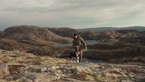 hiker with alaskan malamute over craggy terrain in hildremsvatnet lake, norway