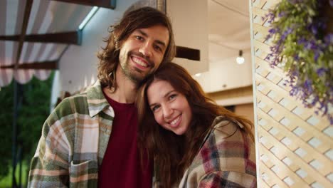 Portrait-of-a-happy-couple,-a-brunette-girl-in-a-plaid-shirt-puts-her-head-on-the-shoulder-of-a-brunette-guy-with-stubble-in-a-green-plaid-shirt-and-a-red-T-shirt-during-their-vacation-in-the-camp-near-a-trailer-near-a-picnic-outside-the-city-in-the-summer