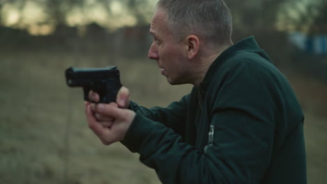 una vista cercana de un hombre apuntando una pistola con ambas manos, con una visión borrosa de los alrededores y una vista borrosa del edificio y el objeto alrededor
