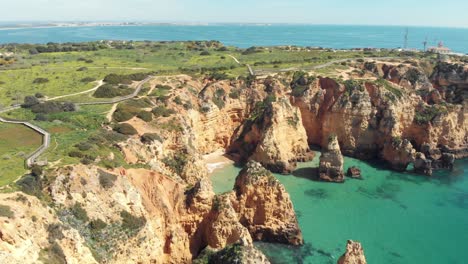 emerald green sea bathing ponta da piedade cliffs in lagos algarve, portugal - wide establishing slide tilt-up shot