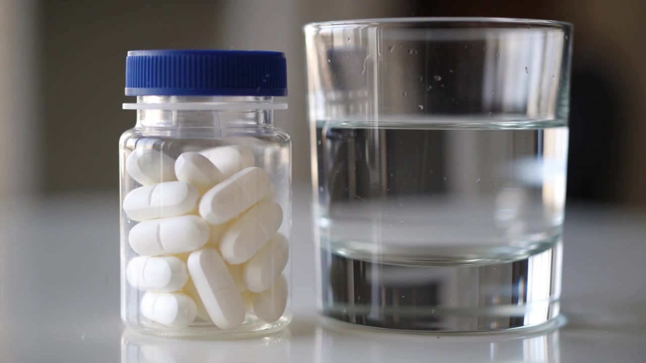 Shifting camera showing pill bottle tablets blue-cap and water-glass on counter for ad, copy space