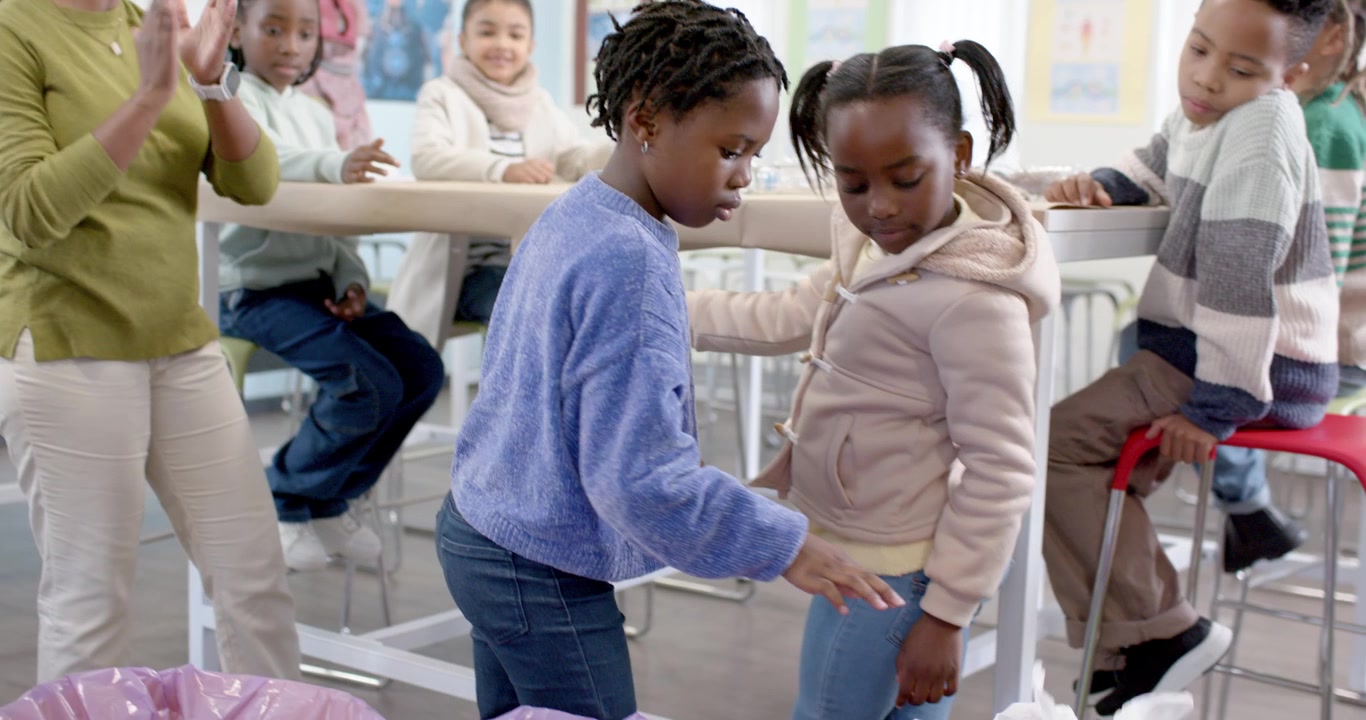 Insegnante afroamericana che insegna ai bambini, sollevando plastica strappata e smistandola nei contenitori per il riciclo