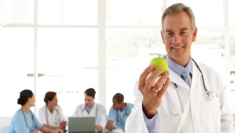 mature doctor looking at camera holding an apple