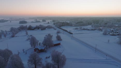 Toma-Aérea-De-Establecimiento-De-Un-Paisaje-Rural,-Campo,-Campos-Agrícolas-Y-árboles-Cubiertos-De-Nieve,-Clima-Helado,-Resplandor-De-Luz-De-Hora-Dorada,-Tiro-Amplio-De-Drones-Moviéndose-Hacia-Atrás