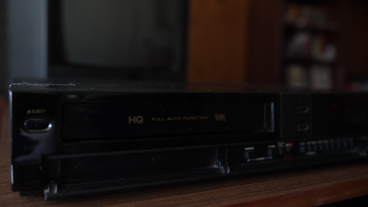 la giovane donna estrae il nastro vhs dal videoregistratore, primo piano statico in camera oscura retrò