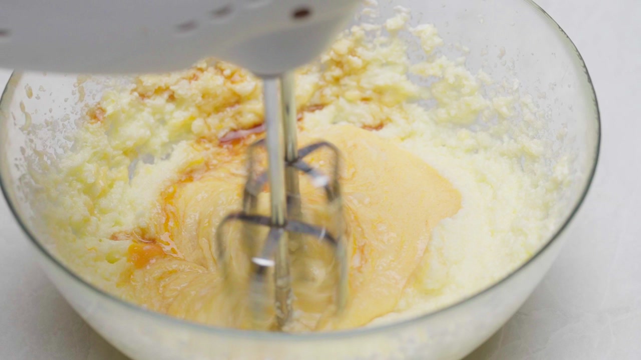 Top down view of electric mixer blending eggs into cookie dough