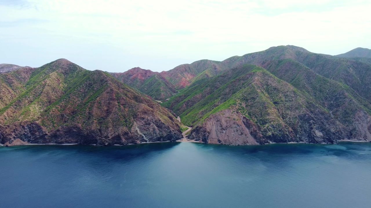 Lunga ripresa aerea in 4K con tracking che rivela le creste vulcaniche stratificate verdi e marroni dell'isola di Cerralvo accanto alle acque blu profonde della Baia di La Ventana, Bassa California del Sud, Messico.