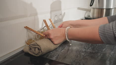 hand view of lady with bracelet adjusting three glass cups near a tilted wall with an electric outlet nearby, placing them gently with a thoughtful touch in modern kitchen