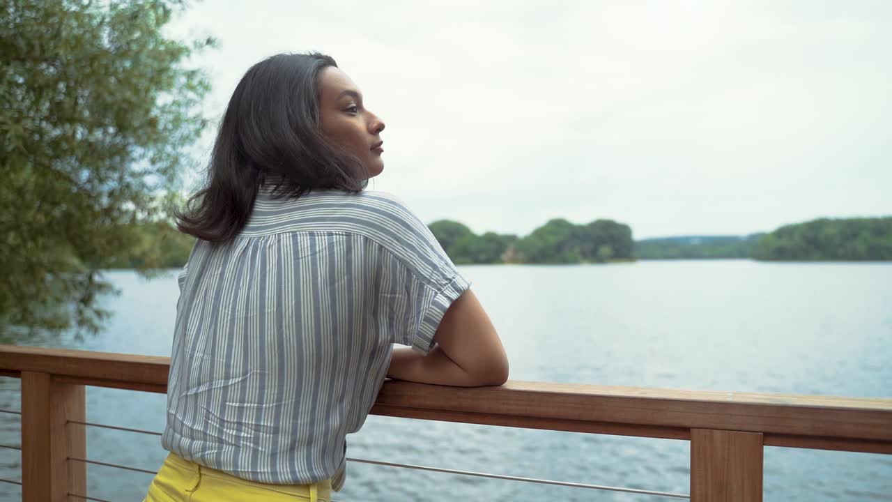 hermosa mujer latina relajada, apoyada en la barandilla del muelle junto al lago tranquilo, cierra los ojos para respirar profundamente, inhalar y exhalar, toma en cámara lenta