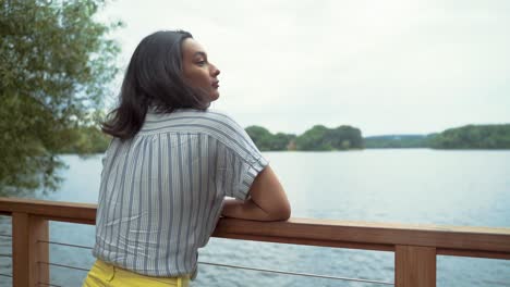 Hermosa-Mujer-Latina-Relajada,-Apoyada-En-La-Barandilla-Del-Muelle-Junto-Al-Lago-Tranquilo,-Cierra-Los-Ojos-Para-Respirar-Profundamente,-Inhalar-Y-Exhalar,-Toma-En-Cámara-Lenta