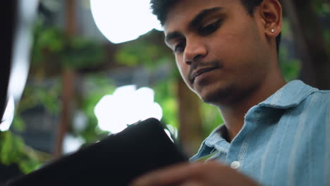 filming young adult with black fluffy hair in indoor space subtle head tilt viewing screen soft ambient light highlighting hair texture candid camera pan capturing relaxed reflective expression