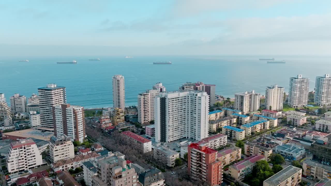 Sorvolo di edifici alti nel centro di Viña del Mar, verso l'Oceano Pacifico con navi da carico in mare.