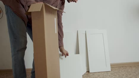 a man takes pieces of furniture out of a box to assemble. close-up on the hands with the goods. saving the family budget