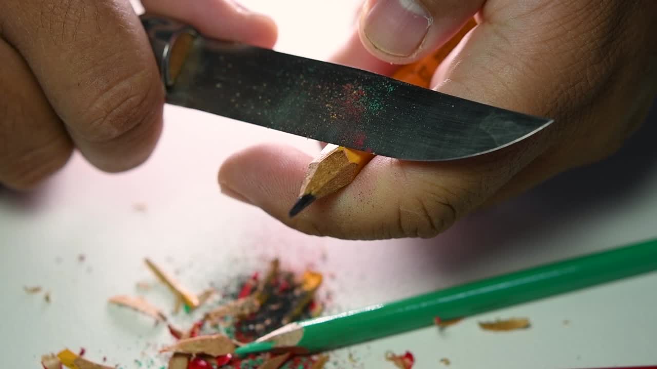 Opptak av hender som sakte spisser en blyant og noen fargeblyanter med en skarp kniv