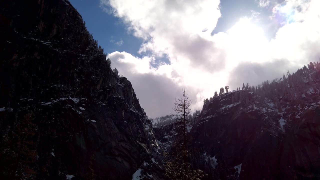 느린 팬, 요세미티 국립공원의 미스트 트레일에 있는 나무가 늘어선 절벽 면의 실루엣을 올려다봅니다.