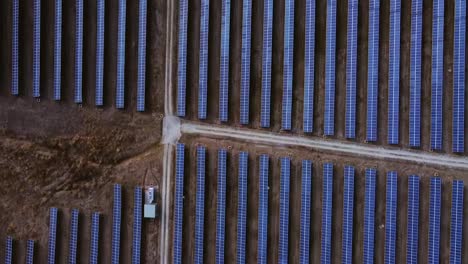 dolly in aerial glides over symmetrical solar panels in a rural farming field