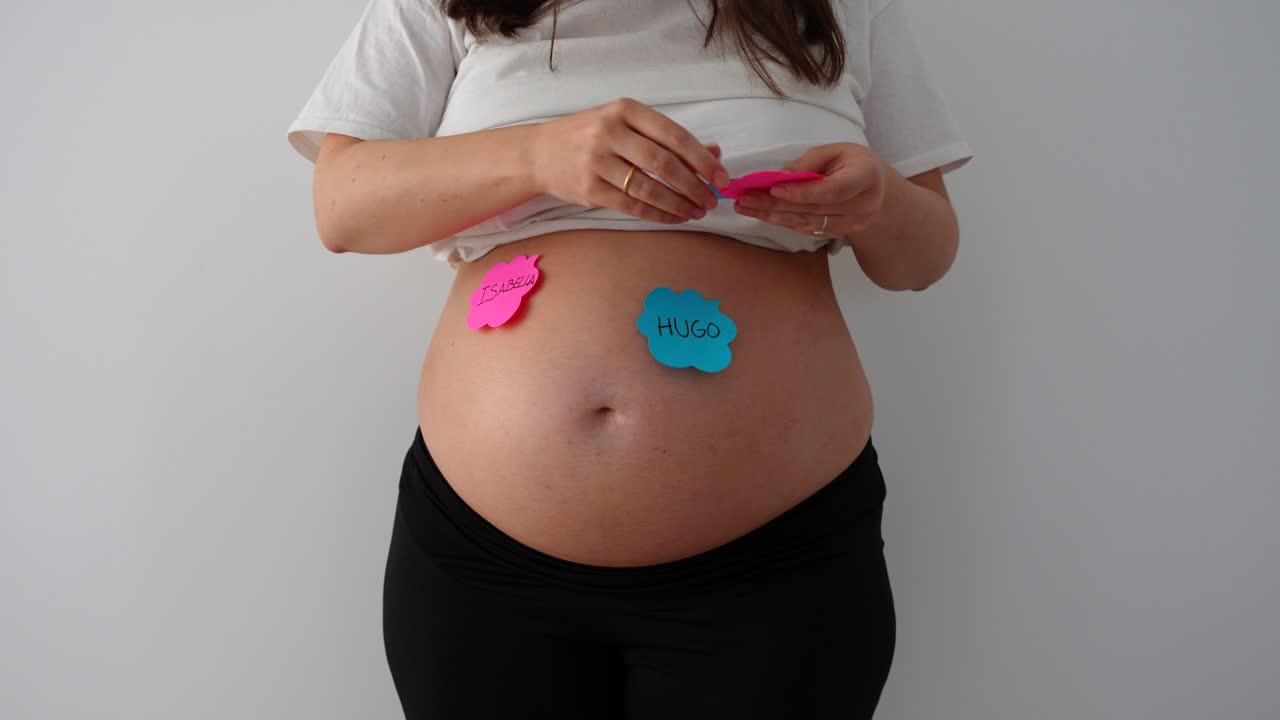 Donna incinta posiziona bigliettini con nomi per bambini sulla pancia durante una sessione di rivelazione del sesso.