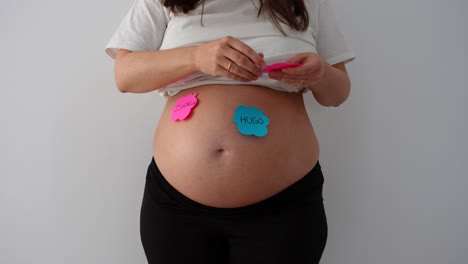 pregnant woman places baby name notes on belly in gender reveal session