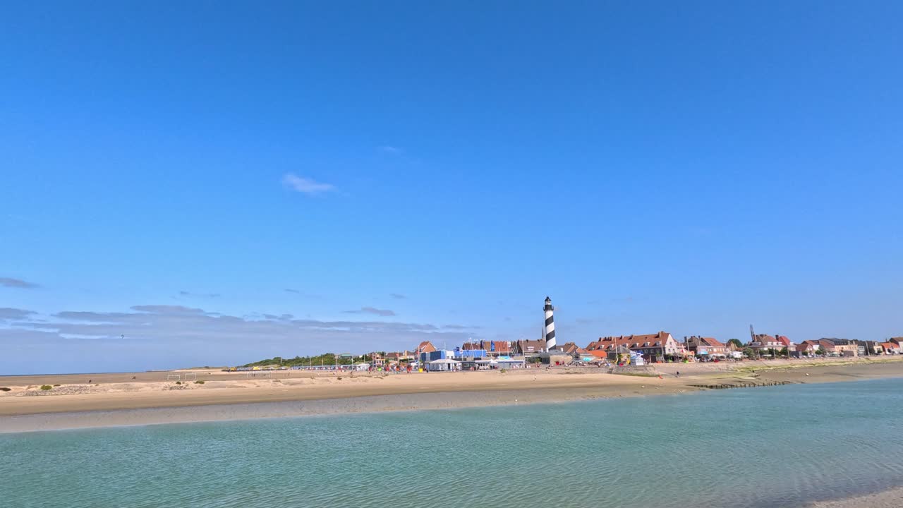 Daytime panoramic video of Gravelines beach, calm sea, striped lighthouse, and clear blue sky