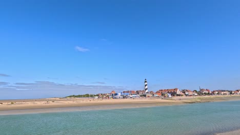 daytime panoramic video of gravelines beach, calm sea, striped lighthouse, and clear blue sky
