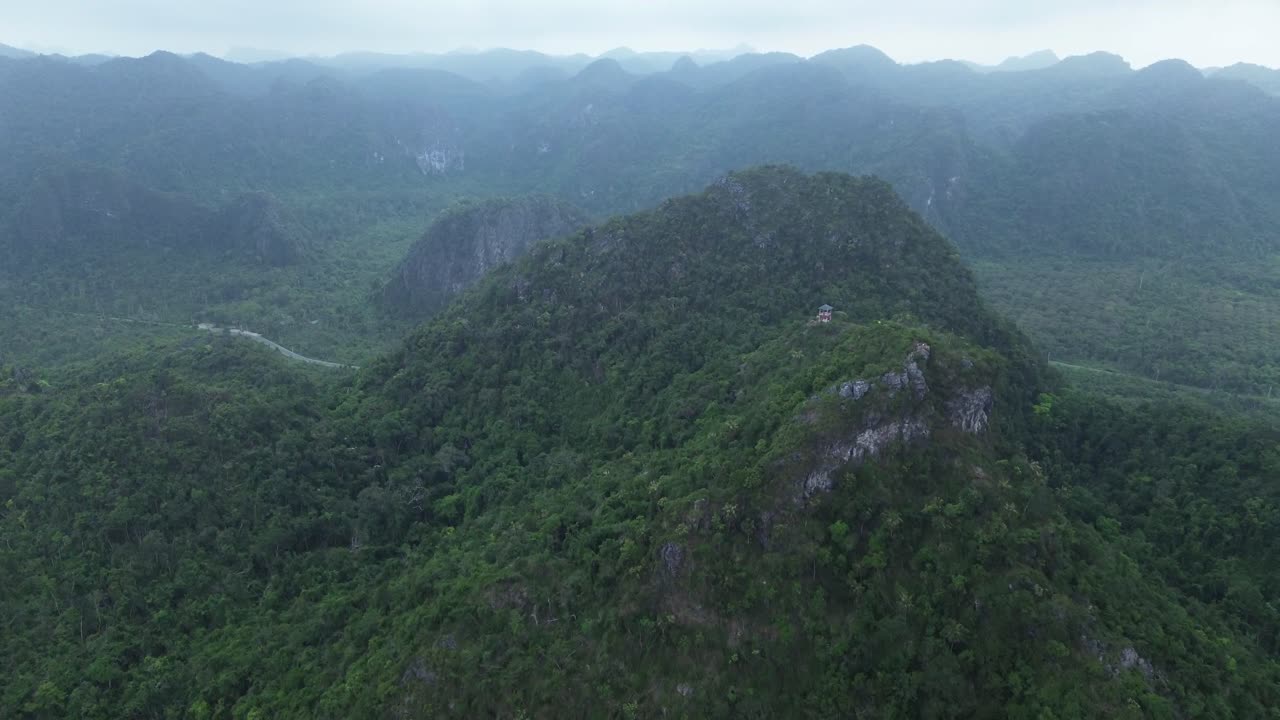 Cinematic drone zoom in over steep green mountain surrounded by dense jungle in Cat Ba