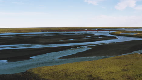 Aerial view flying over a bridge in Iceland, glacial rivers, bridge traffic. Aerial Views of Iceland's Volcanic Delta. Wide open landscape.