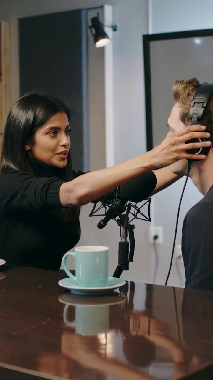 Vertikal video: Kvinde i sort placerer headset og justerer pasformen på vært under studieforberedelse nær mikrofonen